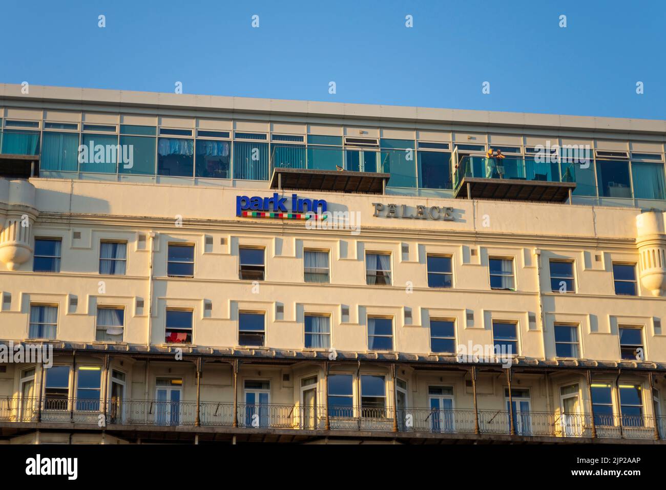 Die Leute blicken vom Balkon aus auf Park Inn Palace, Palace Hotel, Pier Hill, Marine Parade, Southend on Sea, Essex. Am Meer gelegenes Hotel, das am späten Abend erstrahlt Stockfoto