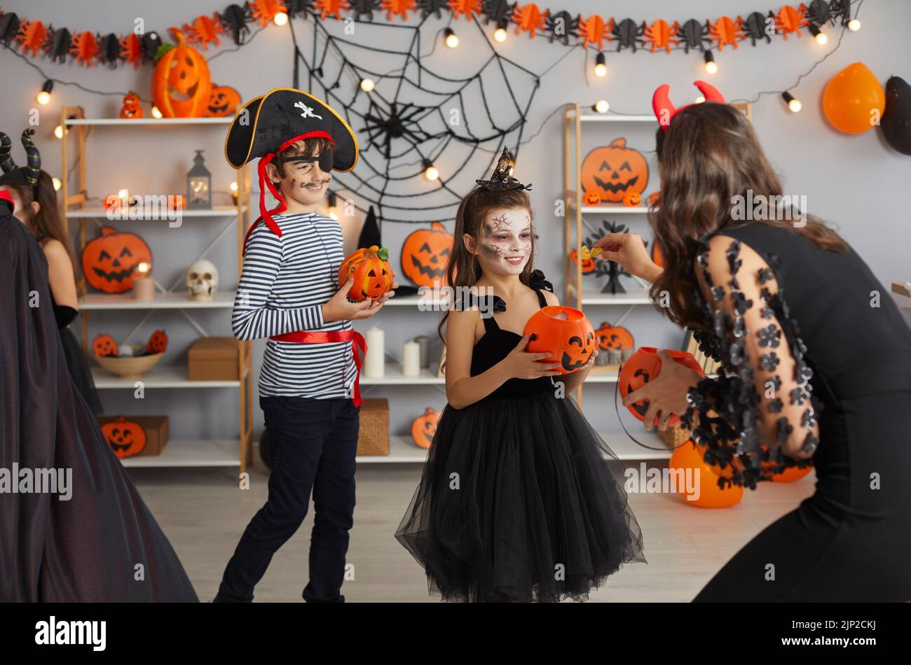 Frau auf der Halloween-Party gibt Süßigkeiten an Kinder, die in gruseligen Maskerade-Kostümen gekleidet sind. Stockfoto