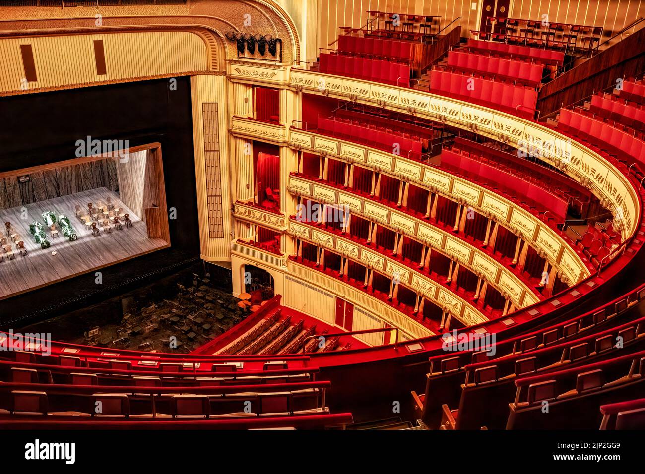 Das Innere der Wiener Staatsoper mit einer hell erleuchteten Bühne und runden Reihen leerer roter Sitze Stockfoto