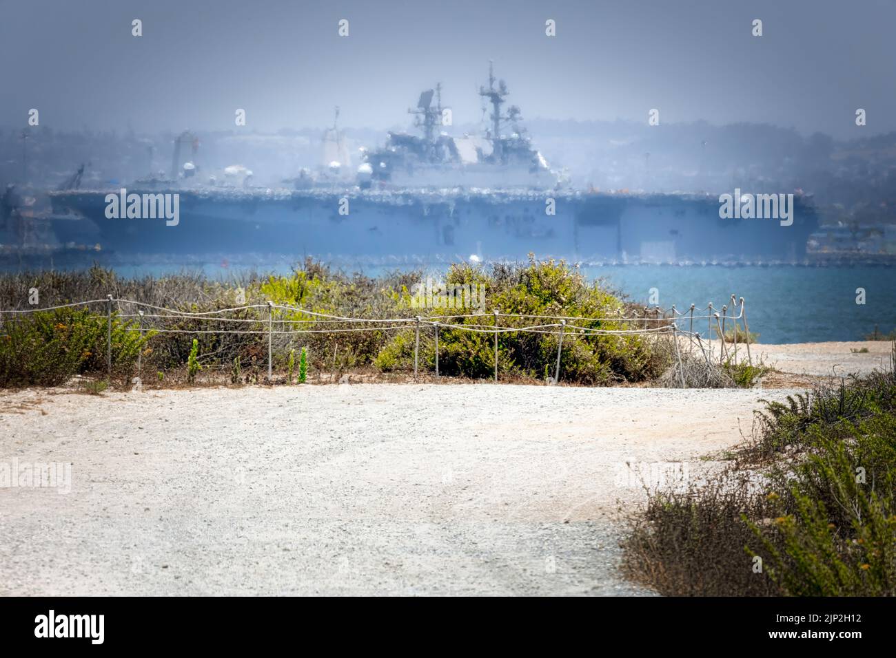 Ein Schotterweg auf dem Silver Strand, südlich von Coronado, Kalifornien, führt zur San Diego Bay mit einem Sturmschiff der US Navy Wasp-Klasse (LHD) im Hintergrund Stockfoto