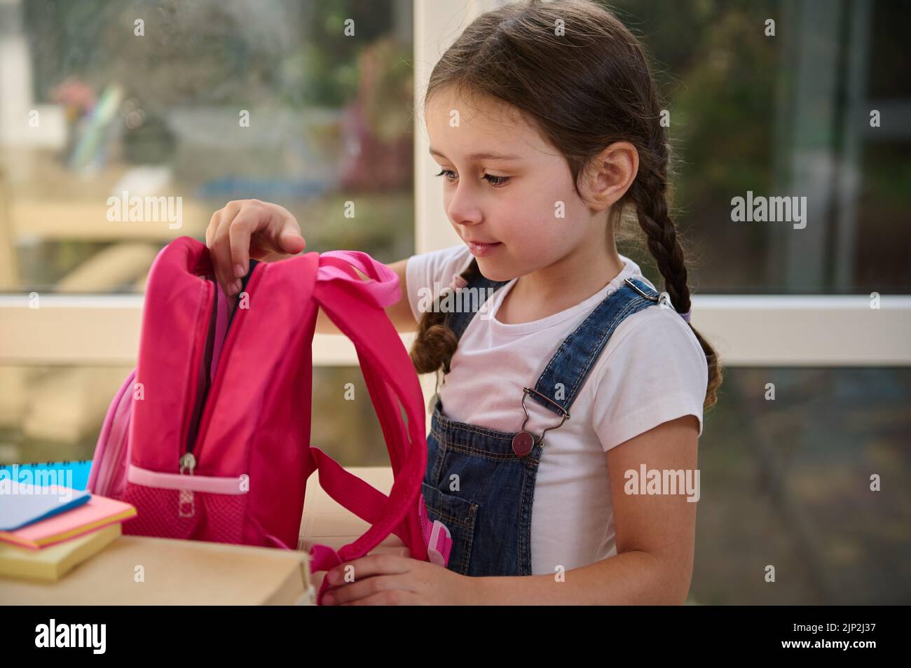 Nahaufnahme eines intelligenten europäischen Schulmädchen, das ihre Schulmaterialien in eine pinke Schultasche legt. First-Grader-Klasse. Zurück zur Schule Stockfoto