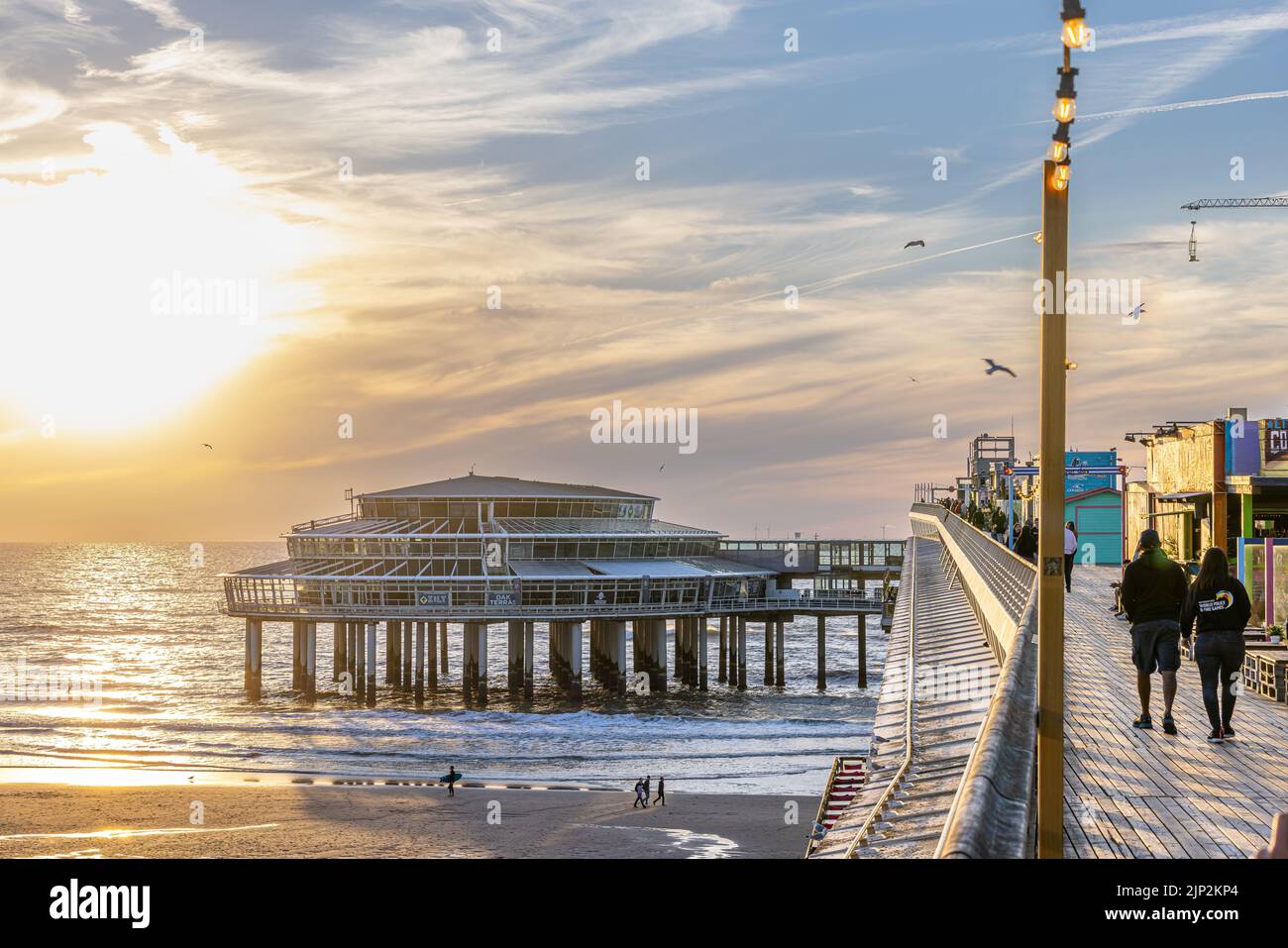 Eine wunderschöne Aussicht auf die Menschen, die während des Sonnenuntergangs auf dem Scheveningen de Pier spazieren gehen Stockfoto