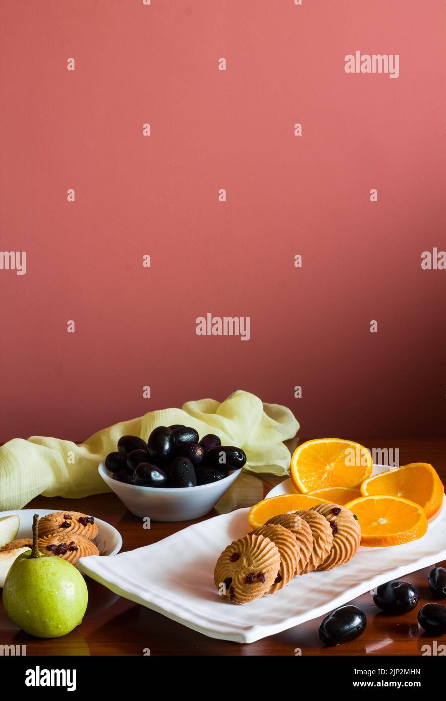 Obstteller mit einer Mischung aus frischen, saftigen, süßen Orangen, Birnen, Jamun, auch als Java-Pflaumenbeeren und Haferkekse bezeichnet, die auf einem dunklen Holztisch als B platziert werden Stockfoto