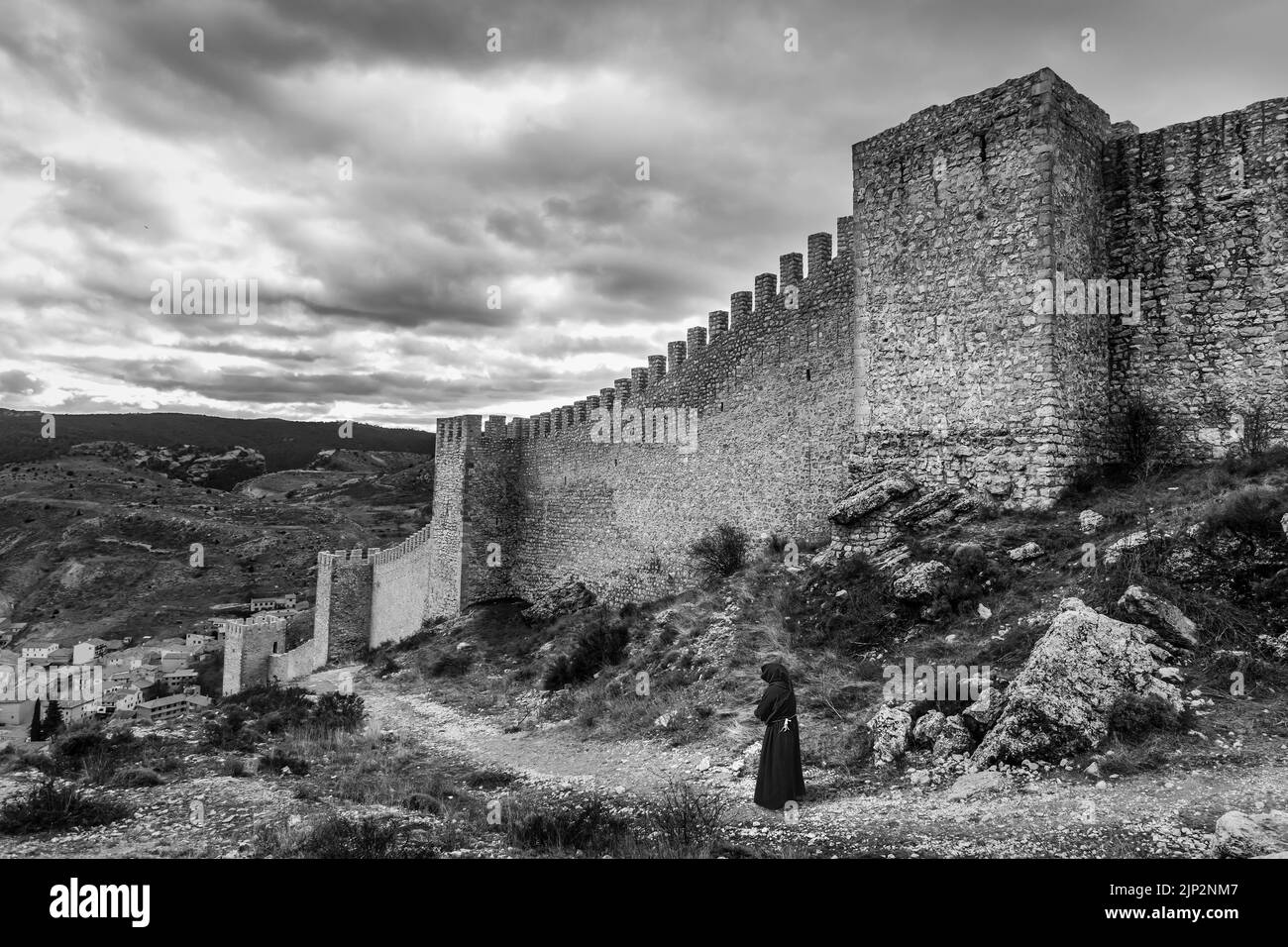Mönch, der auf einem Pfad im Freien läuft, schwarz-weiße Szene mit mittelalterlicher Stadtmauer. Albarracín Teruel Spanien. Stockfoto