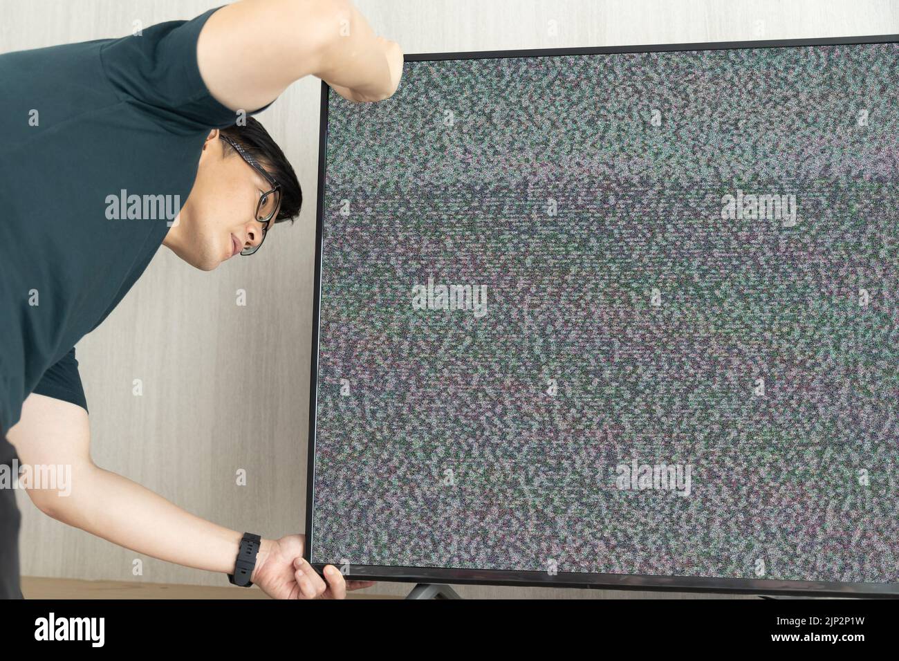 Ein Mann repariert Fernsehen verloren Signalrauschen auf dem Bildschirm suchen Kabel verstecken Stockfoto