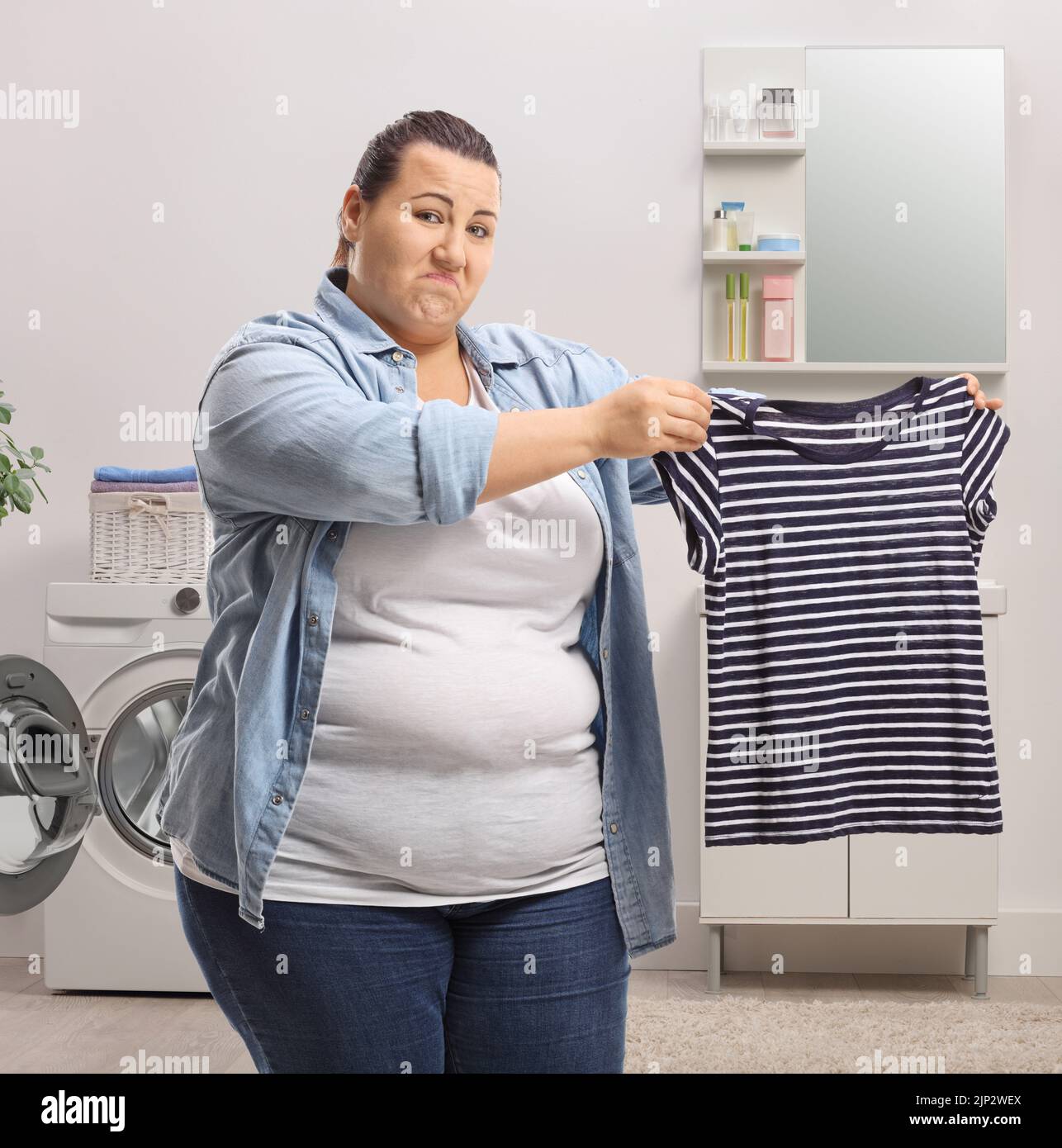 Enttäuschte Frau, die ein geschrumpftes Hemd in einem Badezimmer zeigt Stockfoto