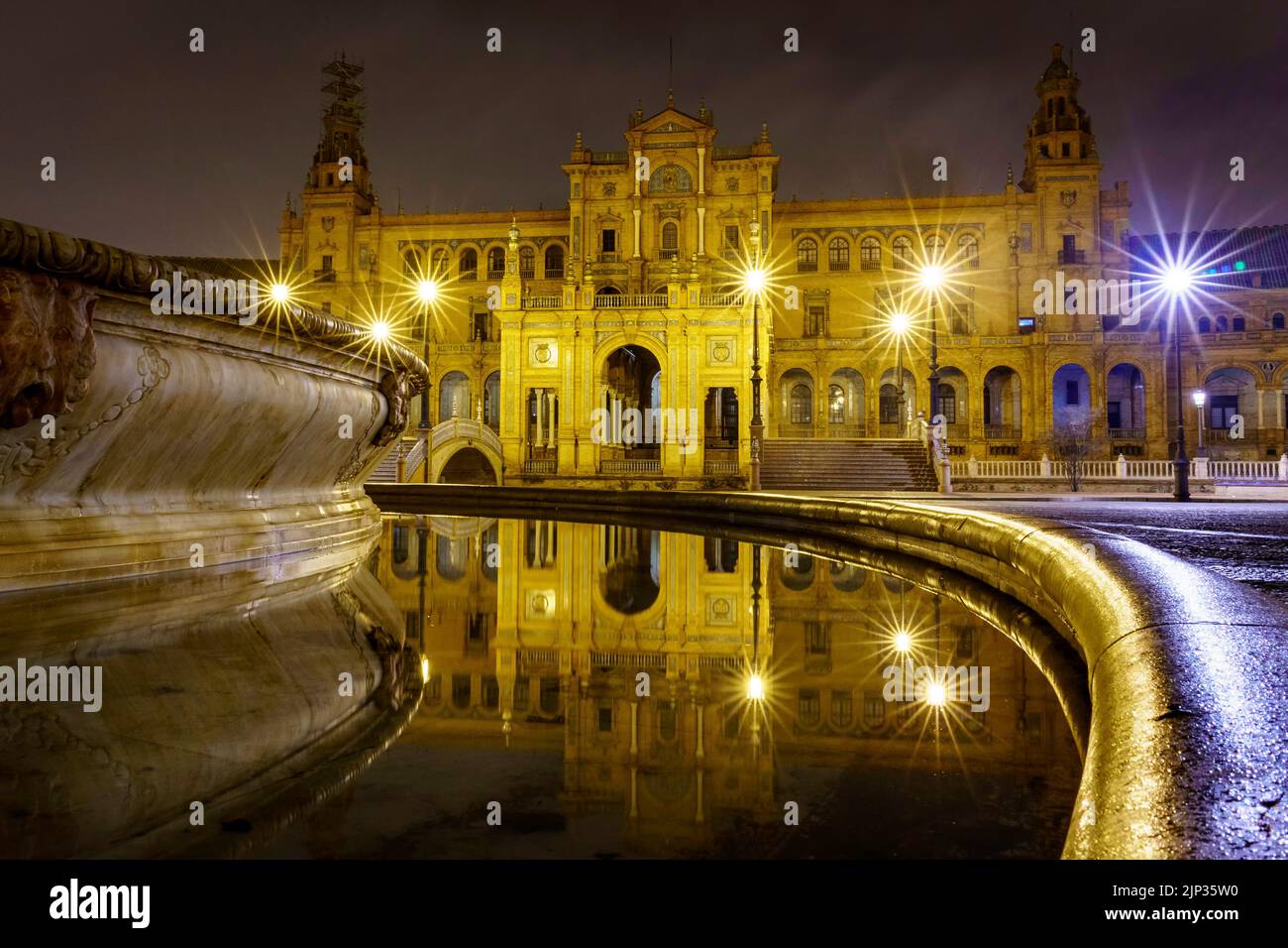Plaza de España in Sevilla, Nachtszene nach Regen mit Langzeitbelichtung Foto und Reflexionen von Lichtern im Wasser und gepflasterten Straßen. Andalusien. Stockfoto