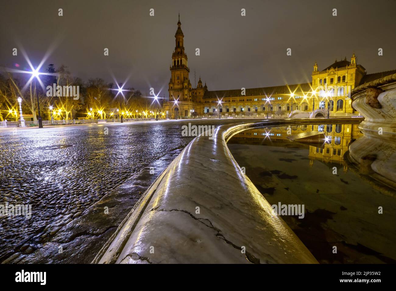 Plaza de España in Sevilla, Nachtszene nach Regen mit Langzeitbelichtung Foto und Reflexionen von Lichtern im Wasser und gepflasterten Straßen. Andalusien. Stockfoto