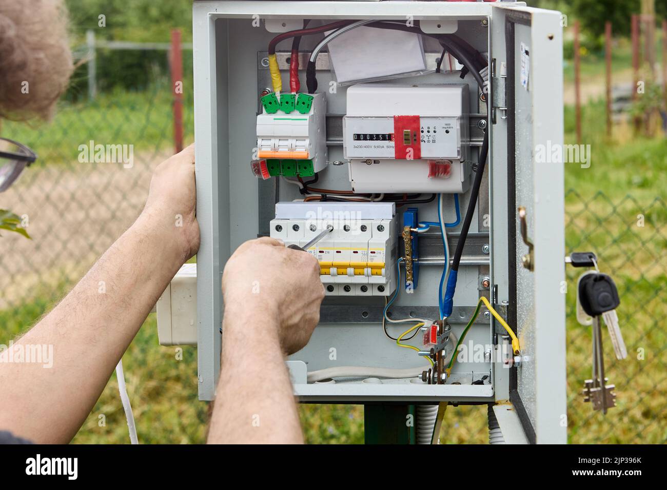 Elektriker befestigt die Anschlussleiste mit einem Kreuzschlitzschraubendreher am Sicherungskasten. Stockfoto