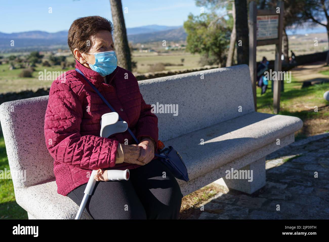 Ältere Frau sitzt auf Parkbank mit sozialer Distanzierung durch Coronavirus. Stockfoto