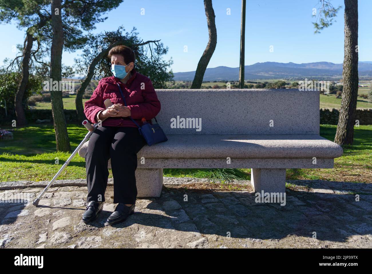 Ältere Frau sitzt auf Parkbank mit sozialer Distanzierung durch Coronavirus. Stockfoto