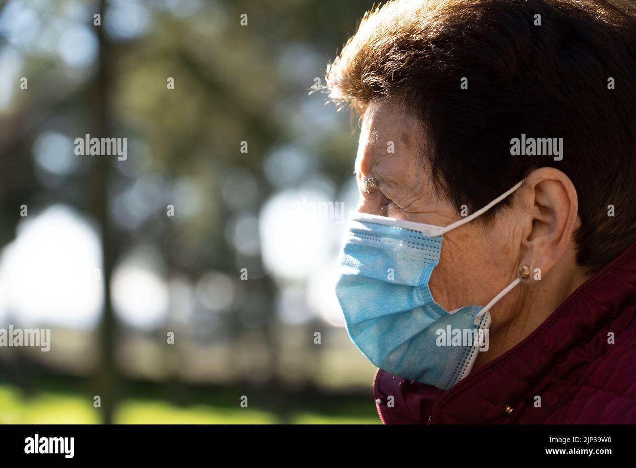 Ältere Frau, die durch den Stadtpark mit einer Maske und sozialer Distanz wegen des Coronavirus spazierend ist. Spanien. Stockfoto