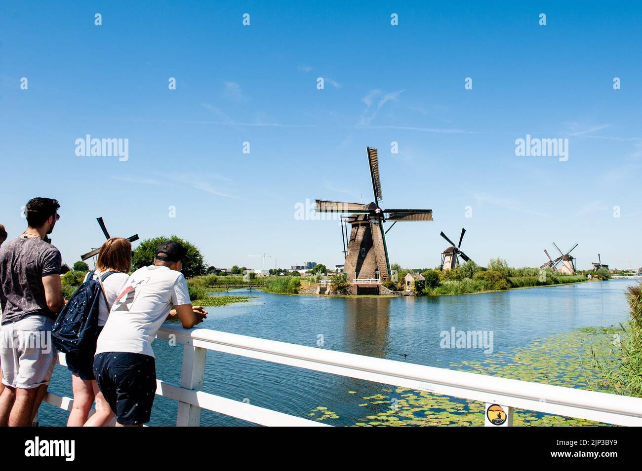 Kinderdijk, Niederlande. 13. August 2022. Besucher werden von einer Brücke aus gesehen, wie sie die Windmühlen betrachten. In der schönen, wasserreichen Gegend in der Nähe von Dordrecht finden Sie die Windmühlen von Kinderdijk. Diese 19 prächtigen Windmühlen, die um 1740 erbaut wurden, stehen dort als Teil eines größeren Wassermanagementsystems, um Überschwemmungen zu verhindern. Heute symbolisieren sie die niederländische Wasserwirtschaft und wurden 1997 zum UNESCO-Weltkulturerbe erklärt. Jedes Jahr besuchen Tausende von Touristen aus der ganzen Welt diesen ikonischen Ort. Kredit: SOPA Images Limited/Alamy Live Nachrichten Stockfoto