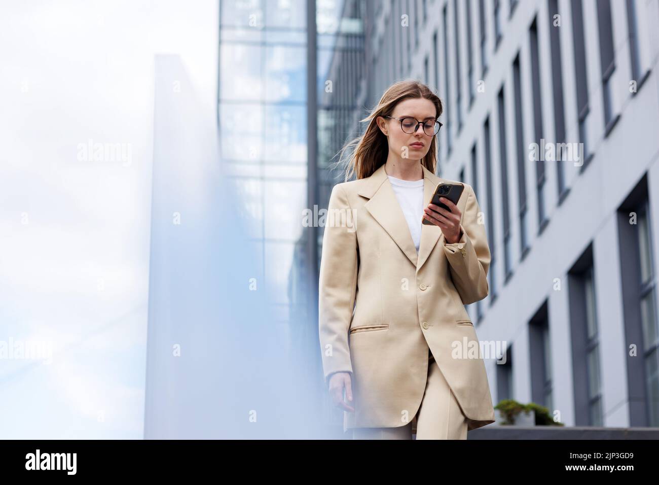 Ein junges blondes Mädchen vor dem Hintergrund eines Geschäftszentrums, Bürozentrums. Unterwegs liest er die Nachrichten von seinem Smartphone. Stockfoto