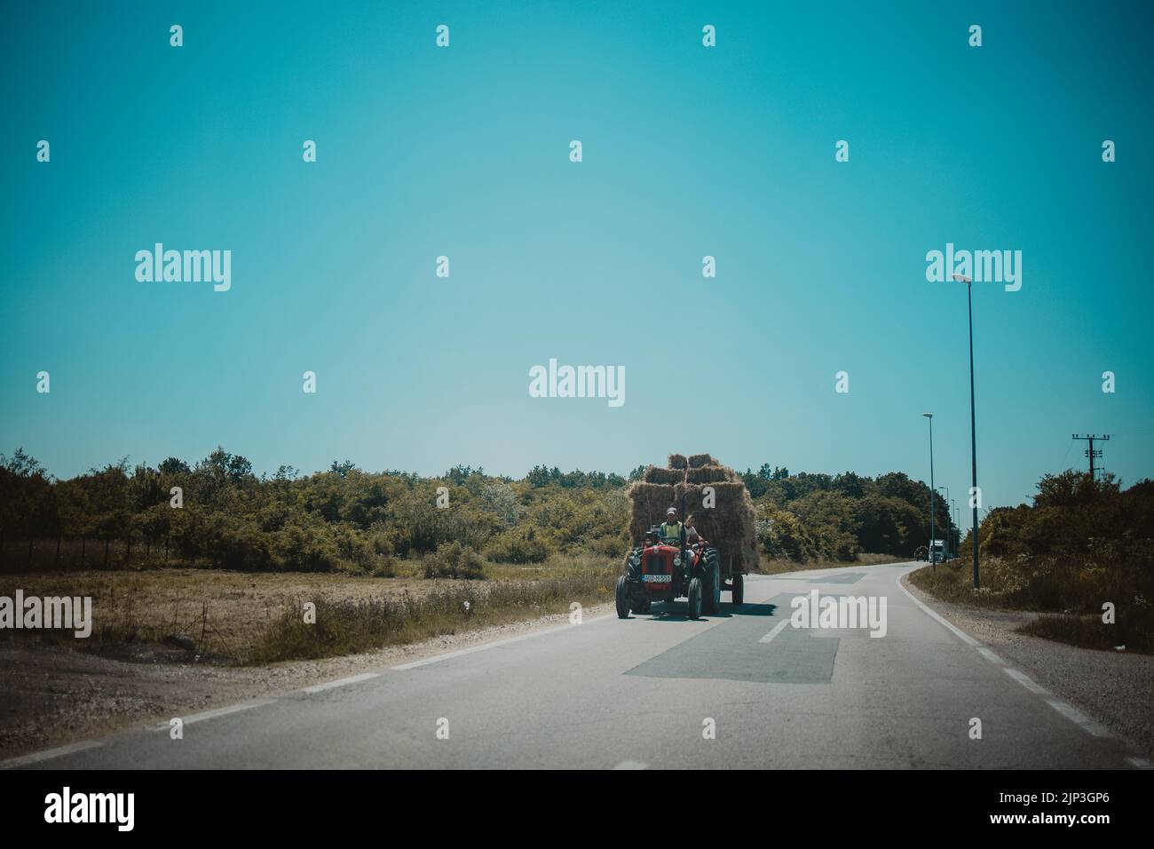 Ein roter Traktor mit Heuballen auf einer Landstraße in Brcko, Bosnien und Herzegowina Stockfoto