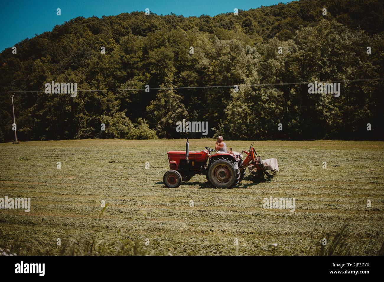 Ein Landwirt auf einem roten Traktor, der auf einem Feld arbeitet Stockfoto
