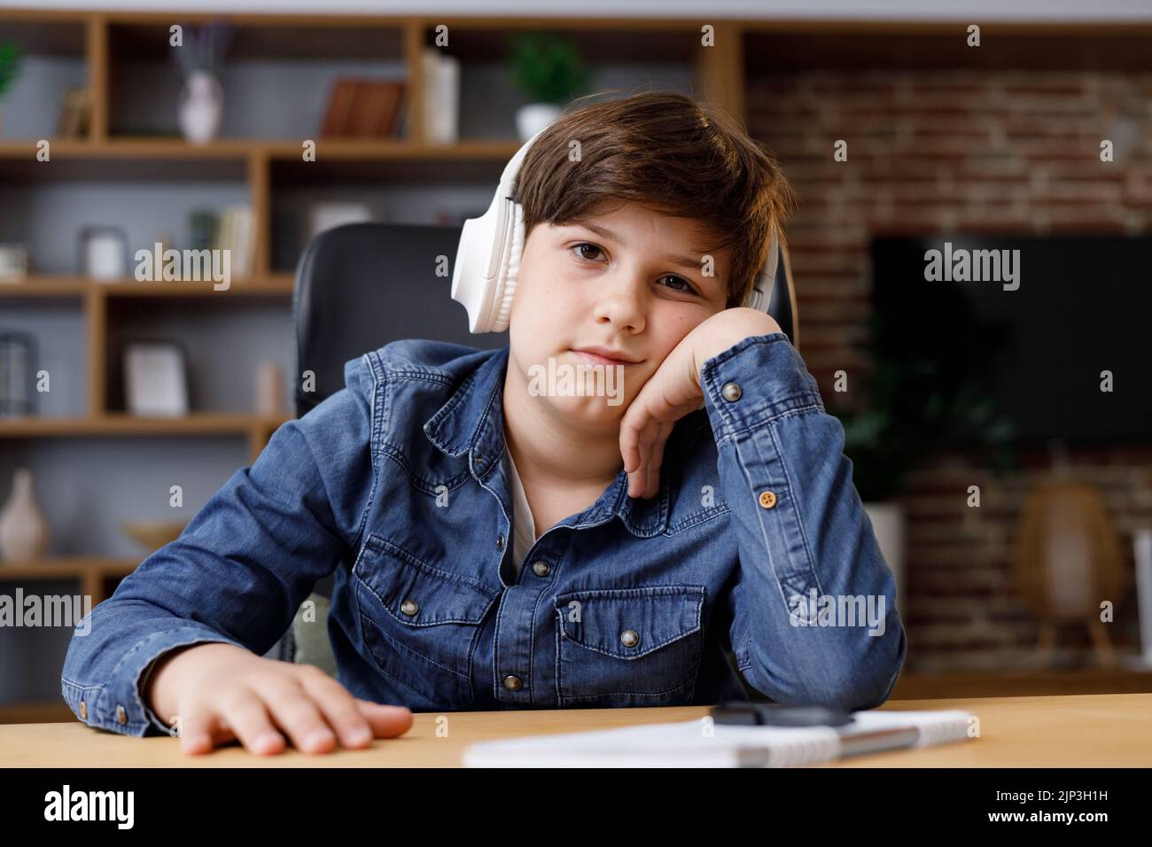 Kleiner Junge, der zu Hause mit einem Laptop fernlernt. Müder Schuljunge, der während einer Online-Lektion mit dem Lehrer einschläft. Fernunterricht ist langweilig und Stockfoto