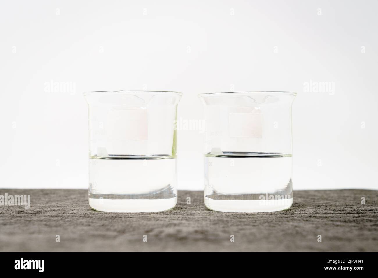 Zwei Becher mit klaren Flüssigkeiten und leeren Etiketten vor weißem Hintergrund Stockfoto