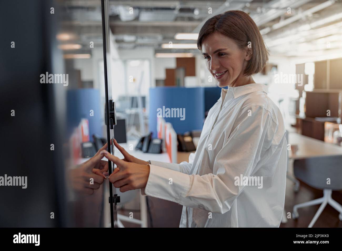 Lächelnde Frau, die ein Passwort oder einen PIN-Code eingibt, um die Sicherheitstür im Büro zu öffnen und zu öffnen Stockfoto