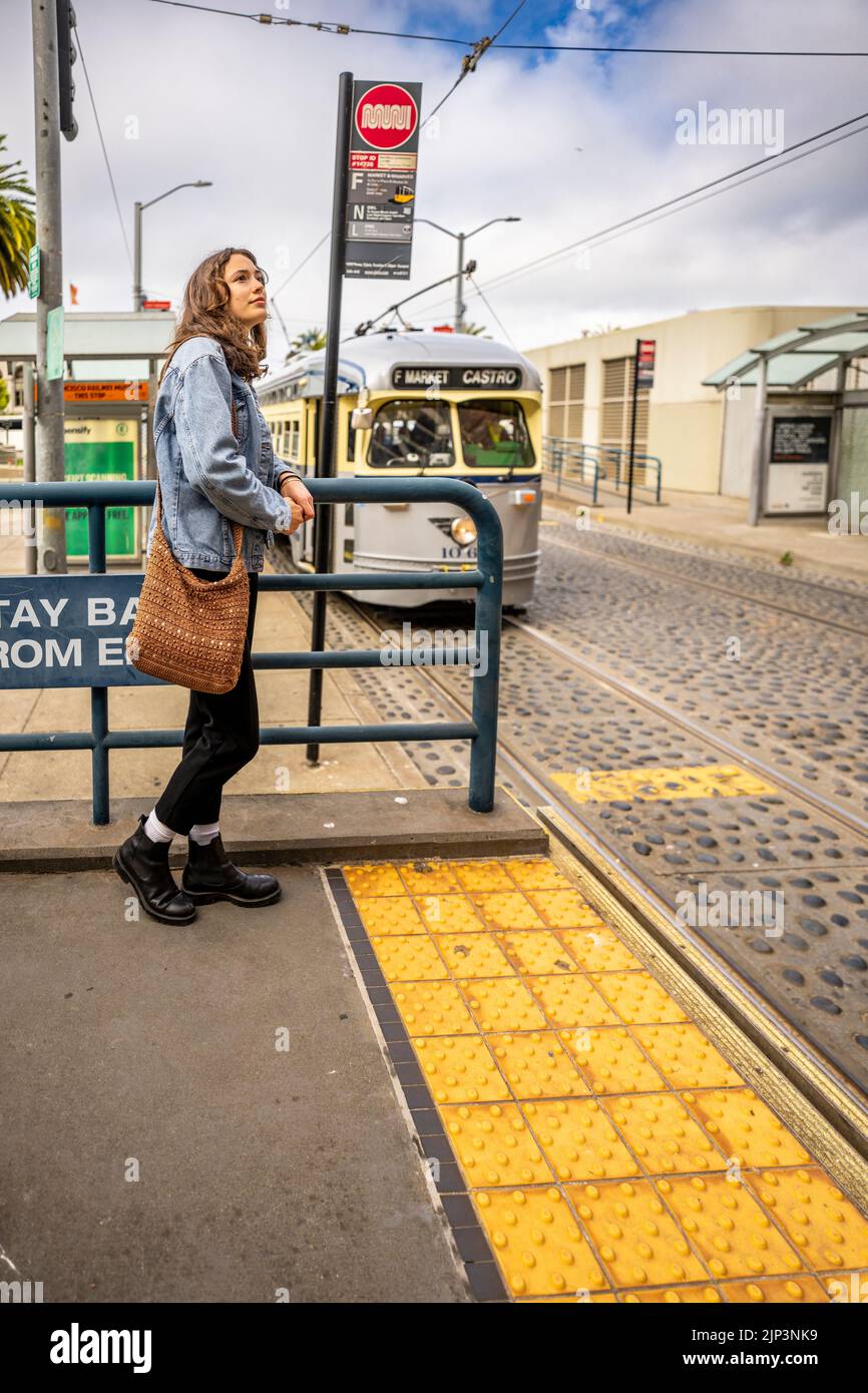 Ungeposistes Porträt einer jungen Frau, die auf öffentliche Verkehrsmittel wartet | San Francisco Muni Stockfoto