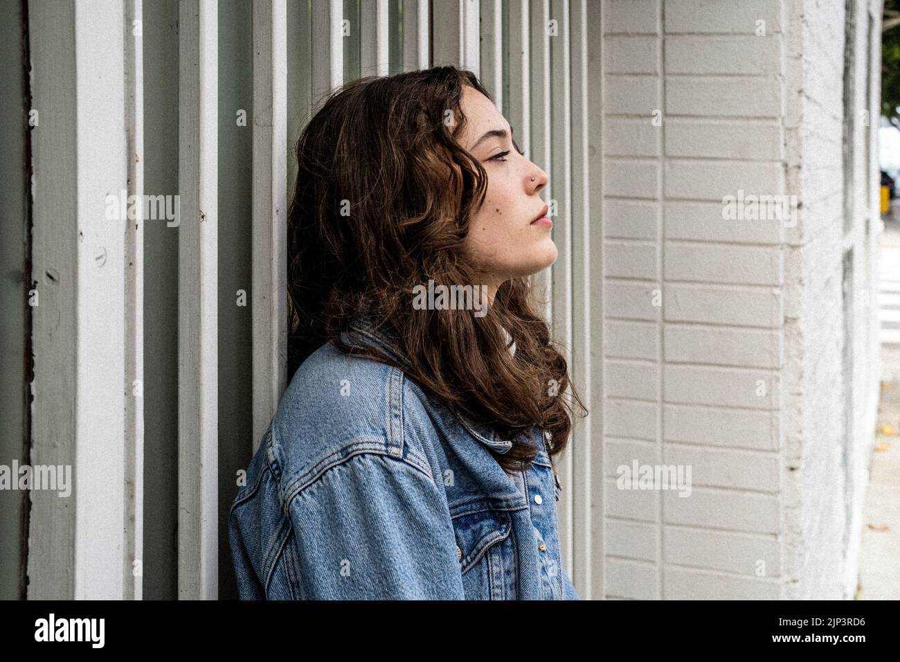 Unbeposed Portrait of Young Woman Waiting at Iron Security Door | Doorway | Downtown Sidewalk Stockfoto