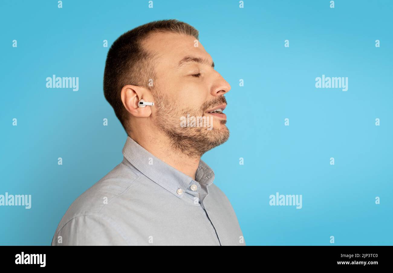 Profil Portrait Of Man Hörmusik Mit Ohrstöpseln, Blauer Hintergrund Stockfoto