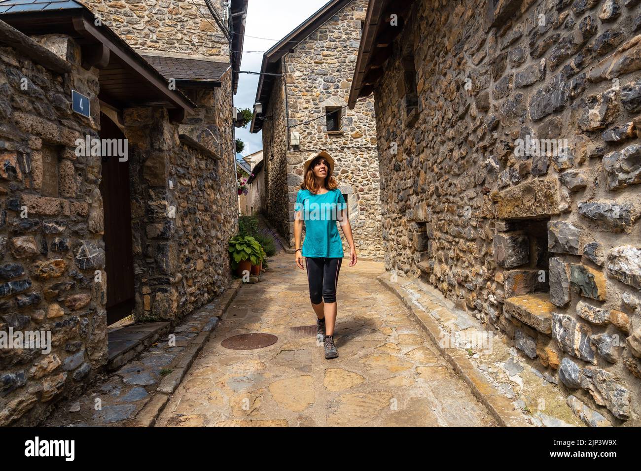 Eine weibliche Touristin in legerer Kleidung, die in einer engen Gasse zwischen alten Häusern in Piedrafita de Jaca spaziert Stockfoto