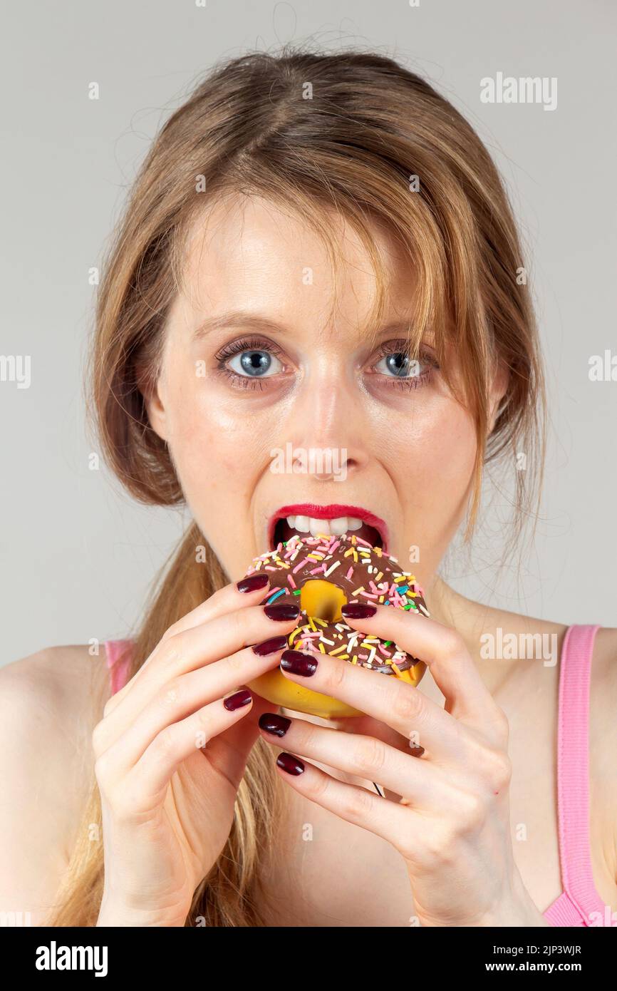 Porträt einer jungen Frau, die auf ungesunde Weise Schokoladendonut isst Stockfoto