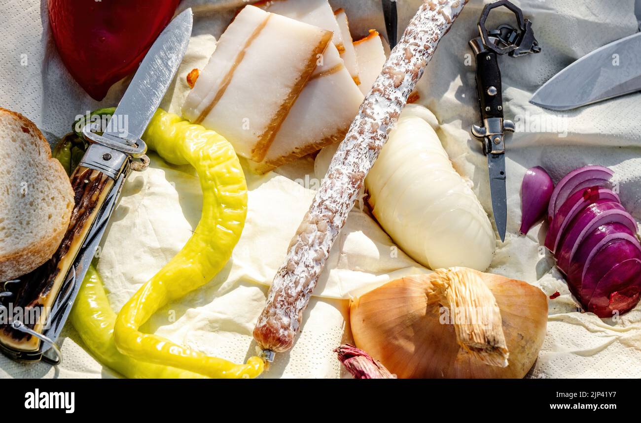 Rumänische traditionelle Küche mit Würstchen, Zwiebeln und Käse, Schinken und Paprika und einem Messer auf einem Handtuch Stockfoto