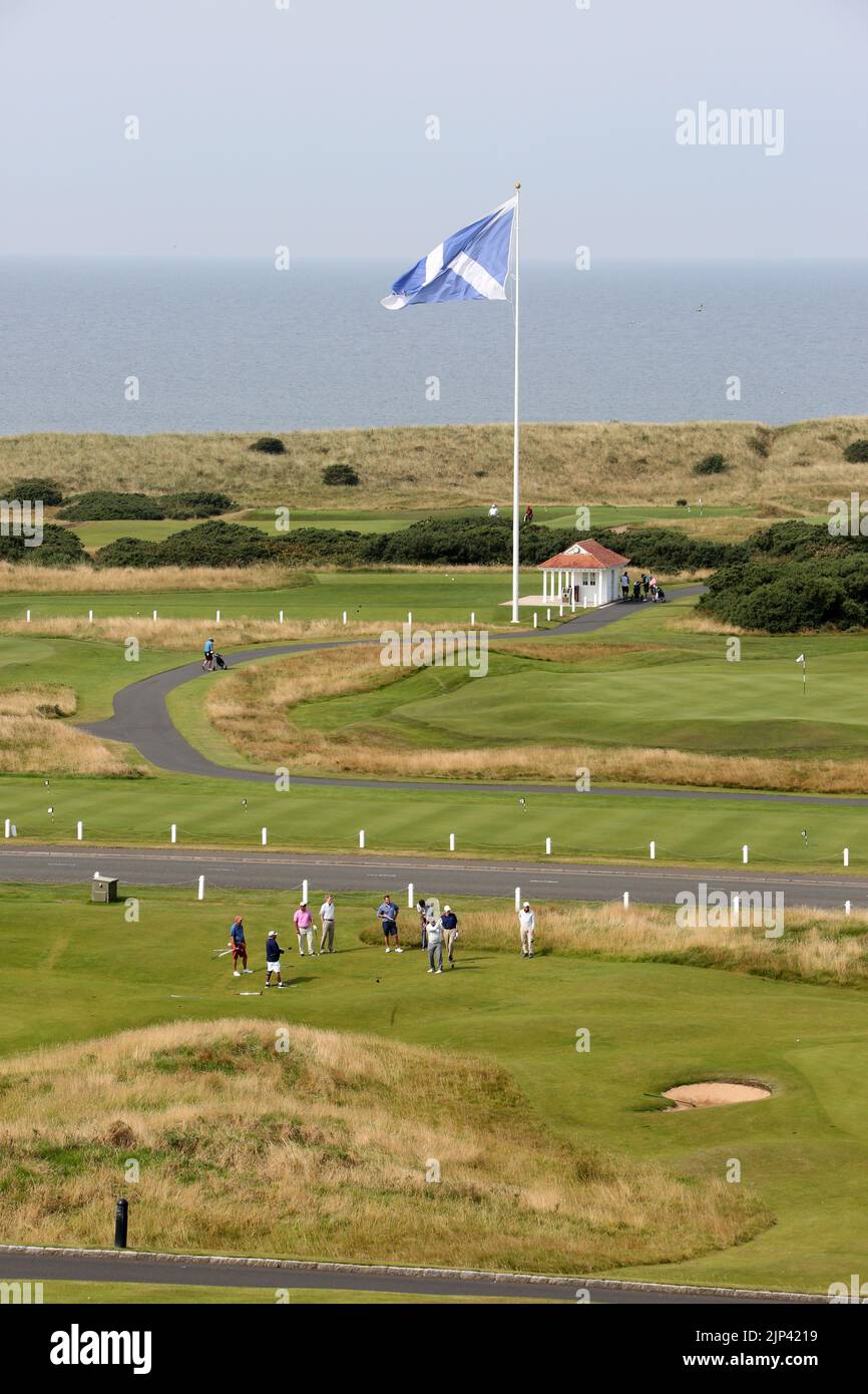 Trump Turnberry, Ayrshire, Schottland Großbritannien.eine der größten Saltire-Flaggen in Schottland dominiert die Gegend und kann von Meilen entfernt gesehen werden. Dieser Blick vom Hotel Turnberry mit der Starterhütte für den ersten Tee, Übungsgreens und das 18. Green. Ebenfalls auf dem Foto ist die ikonische große Uhr zu sehen, die den Namen Donald Trumps trägt Stockfoto