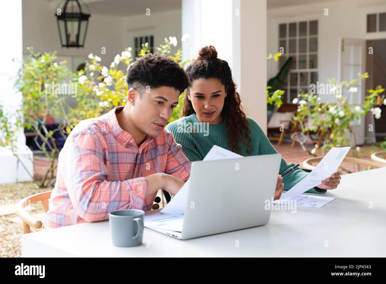 Biracial Paar sitzt auf der Gartenterrasse außerhalb des Hauses mit Laptop und Rechnungen bezahlen Stockfoto