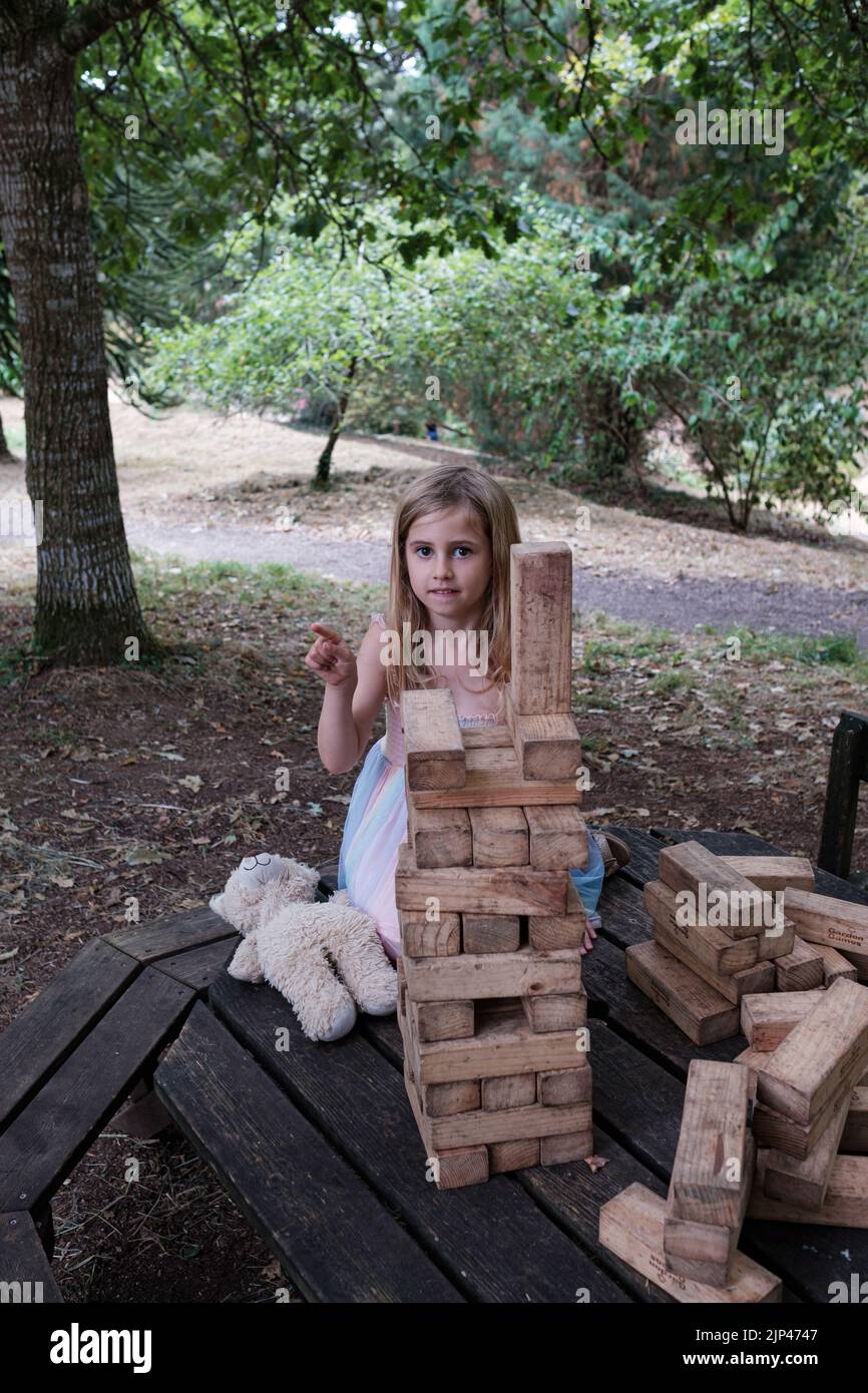 5yr alte Mädchen in rosa und blauen Kleid spielt mit Holzblöcken in Parklandschaft Setting Stockfoto