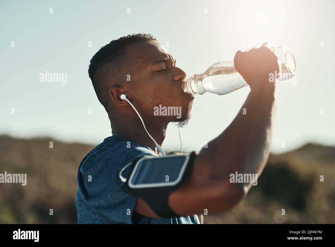 Das Laufen hat mich heiß gemacht, das Wasser kühlt mich ab. Ein hübscher junger Läufer, der eine Pause macht und Wasser im Freien trinkt. Stockfoto