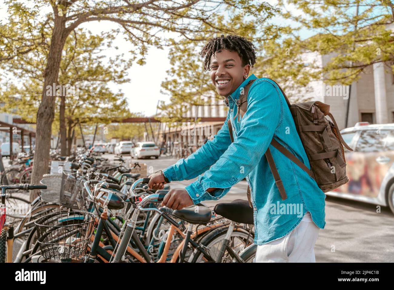 Der Typ berührt das Fahrrad und lächelt der Kamera auf der Straße zu Stockfoto