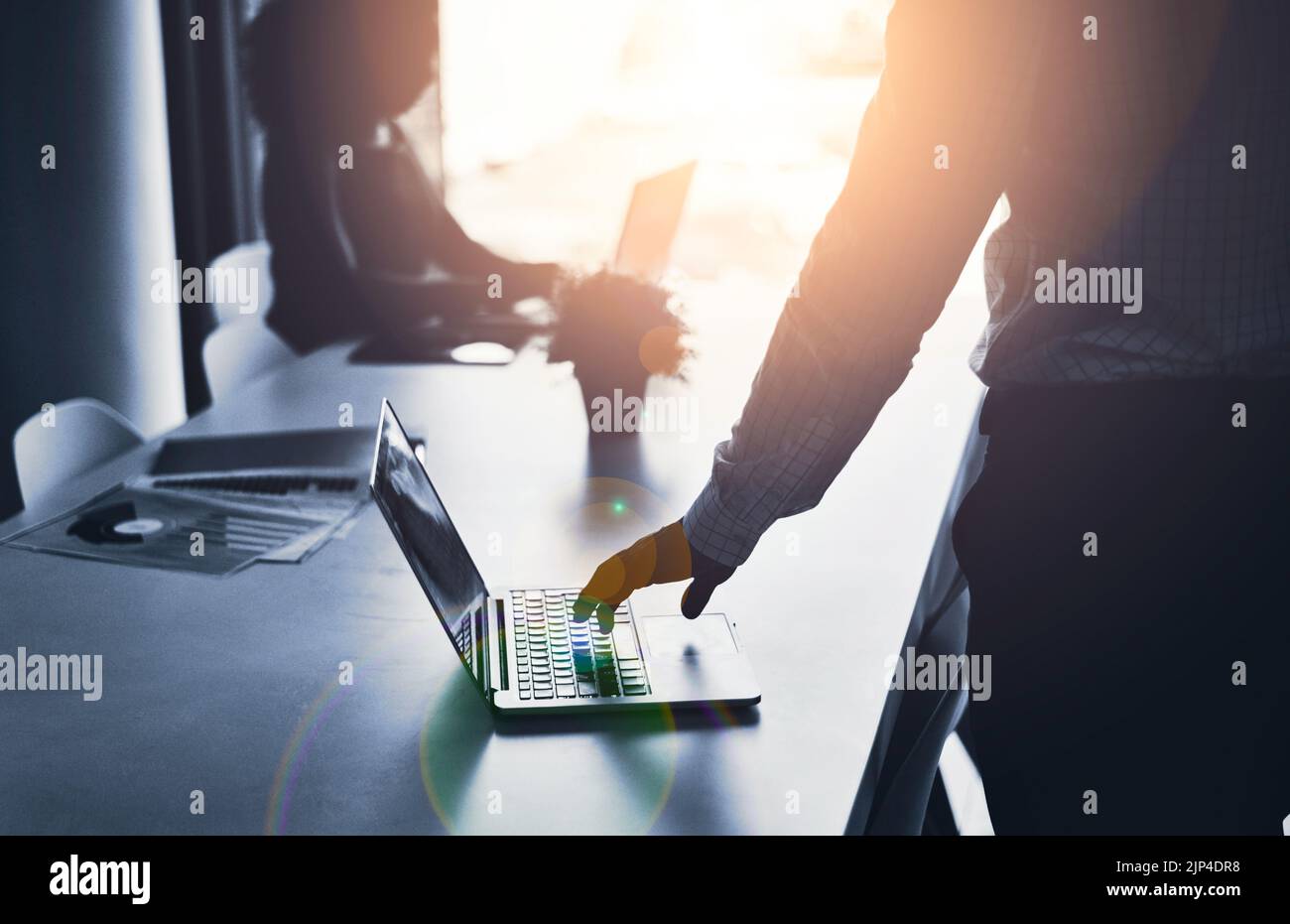 Die Silhouette eines Geschäftsmanns, der in einem IT-Unternehmen an einem Laptop arbeitet und in einem Büro eine Besprechung hat. Ein männlicher Mitarbeiter tippt in einem dunklen Sitzungssaal Stockfoto