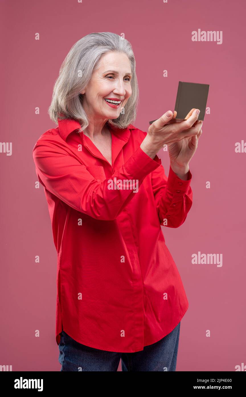 Reife Frau in rot macht Make-up und schaut zufrieden Stockfoto