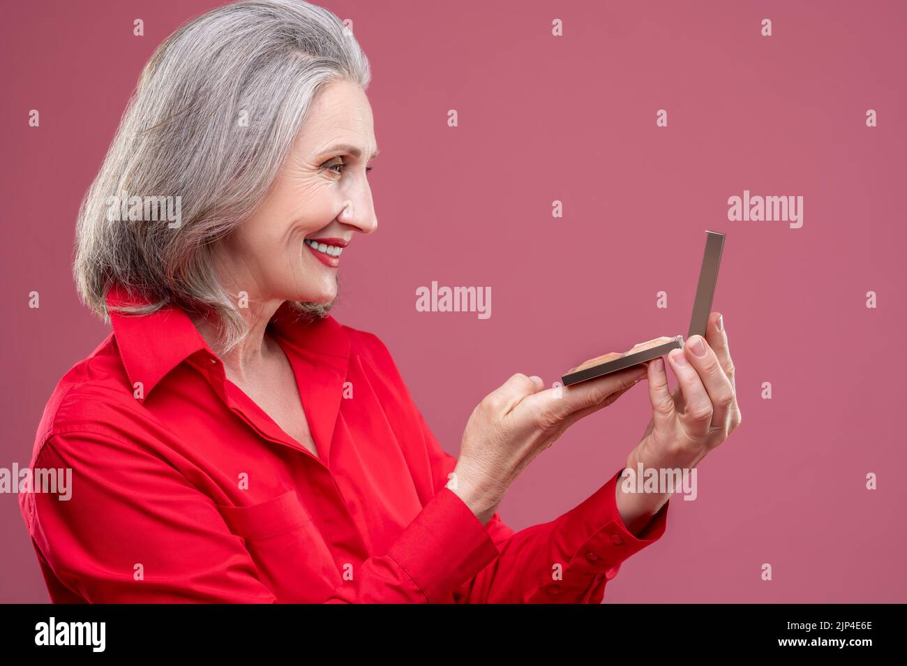 Reife Frau in rot macht Make-up und schaut zufrieden Stockfoto