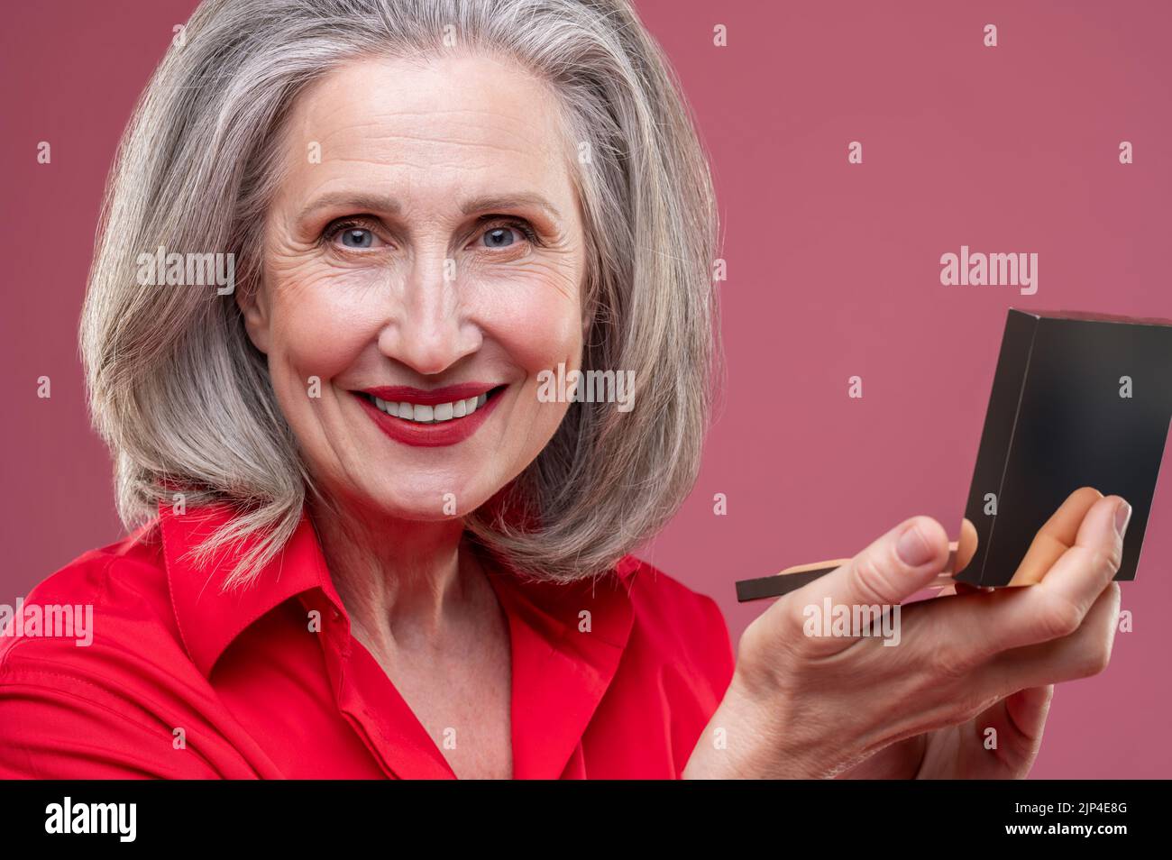 Reife Frau in rot macht Make-up und schaut zufrieden Stockfoto