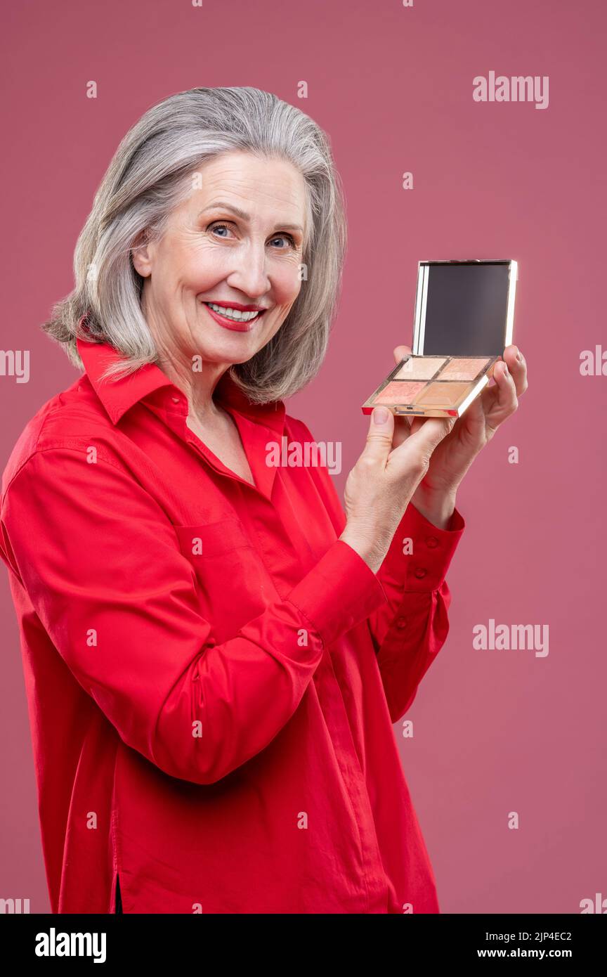 Frau hält die Pulverbox in den Händen und sieht aufgeregt aus Stockfoto