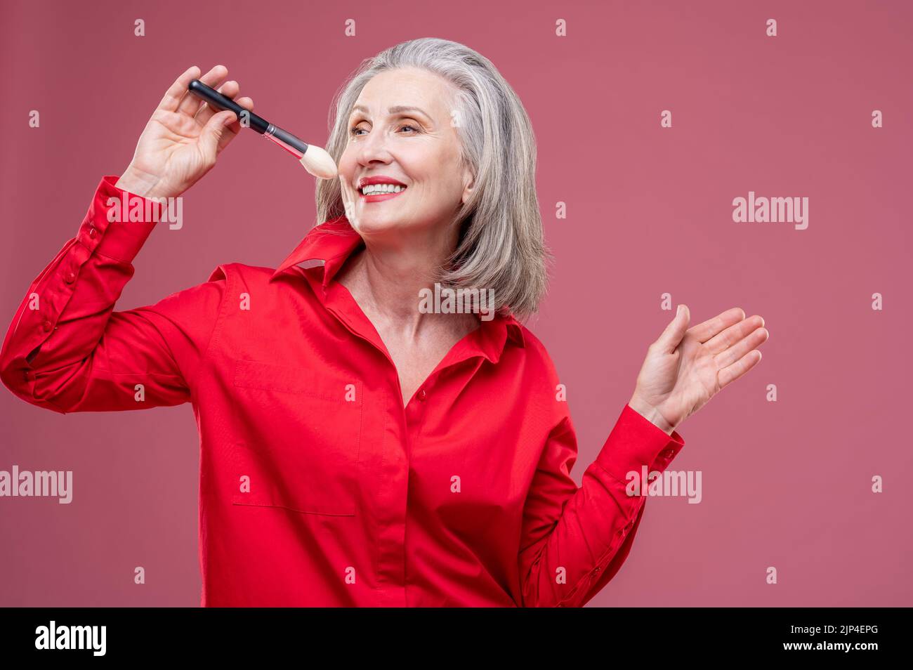 Lächelnde Frau in Rot mit einem Gesichtsbesen in der Hand Stockfoto