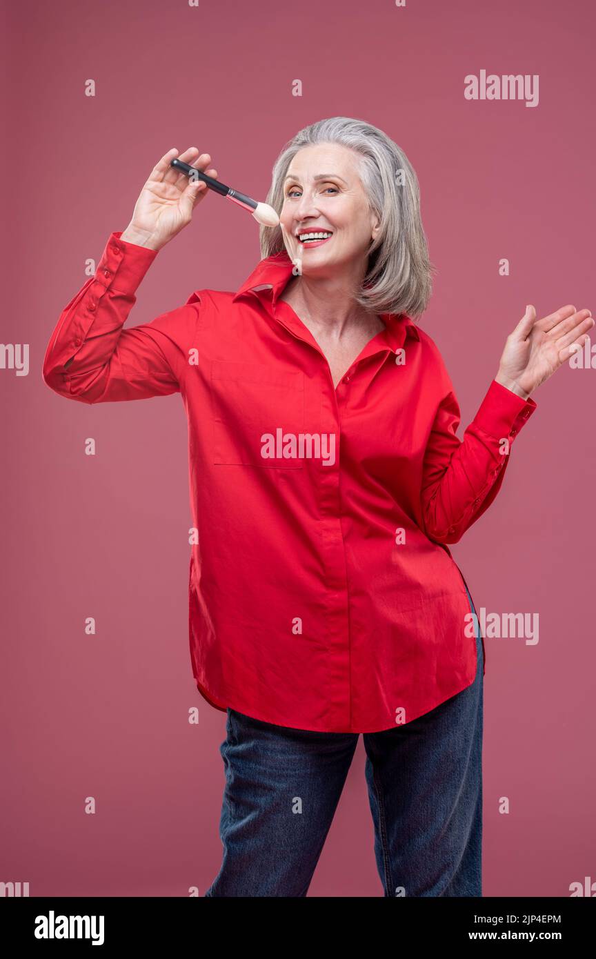 Lächelnde Frau in Rot mit einem Gesichtsbesen in der Hand Stockfoto