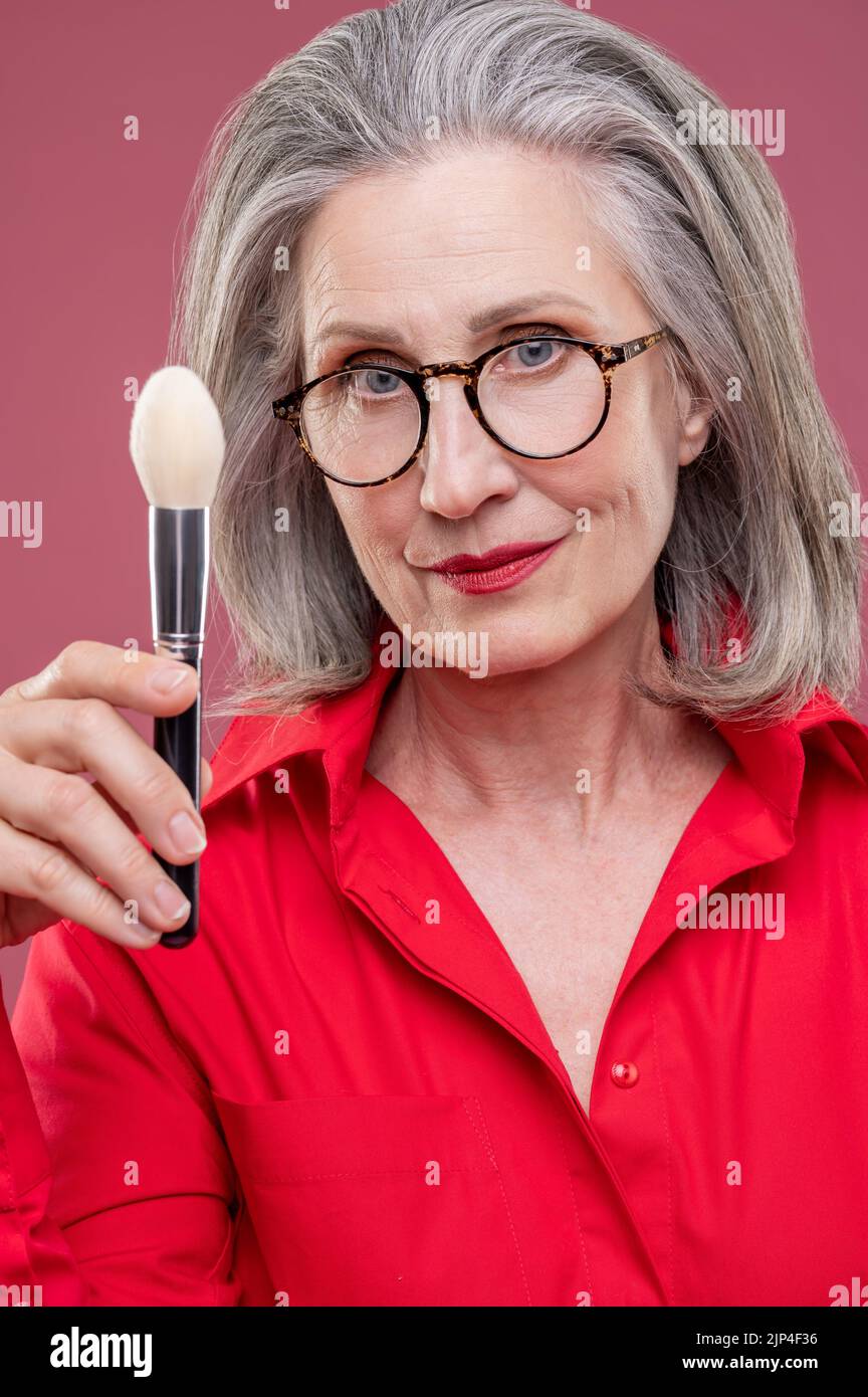 Frau in der Brille woth eine Gesichtsbürste in hnd aussehen nachdenklich Stockfoto