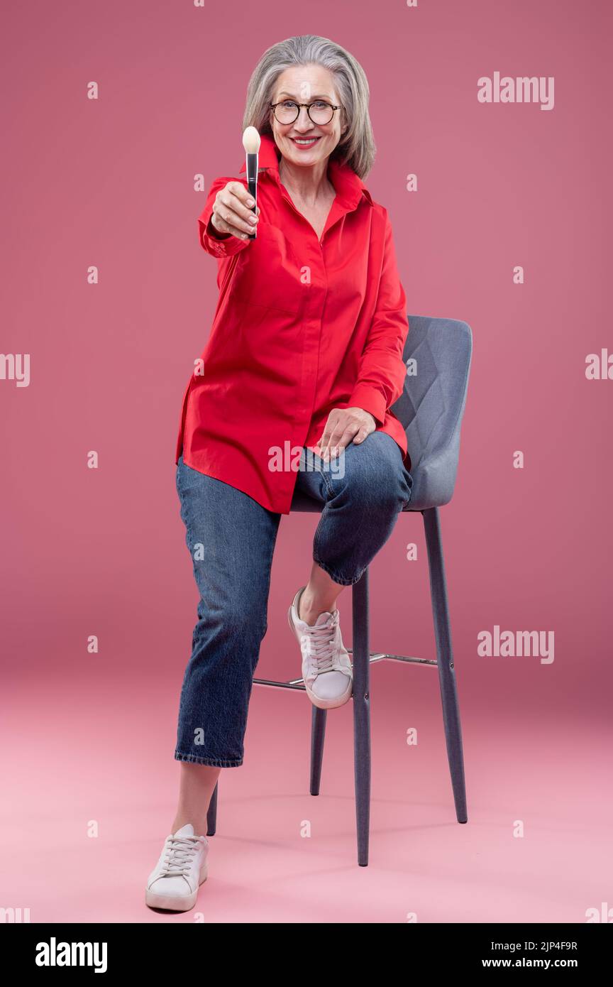 Gut aussehende Frau mittleren Alters in einem Studio, die einen Gesichtsbesen in der Hand hält Stockfoto