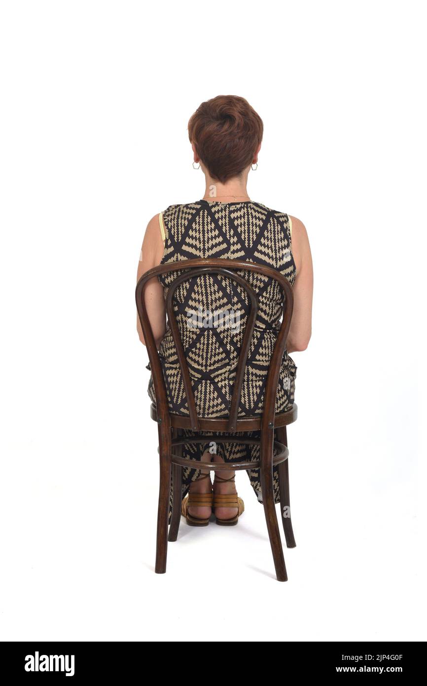 Frau mittleren Alters sitzt von hinten in einem Kleid und Sandalen auf weißem Hintergrund Stockfoto