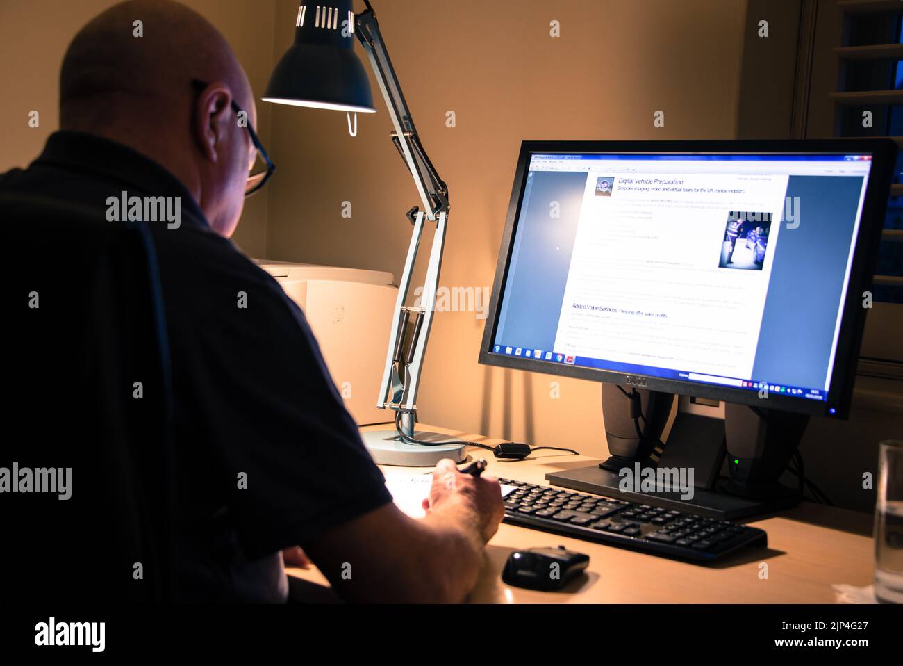 Ein erwachsener Mann mit Brille, der von zu Hause aus vor einem Computer arbeitet Stockfoto