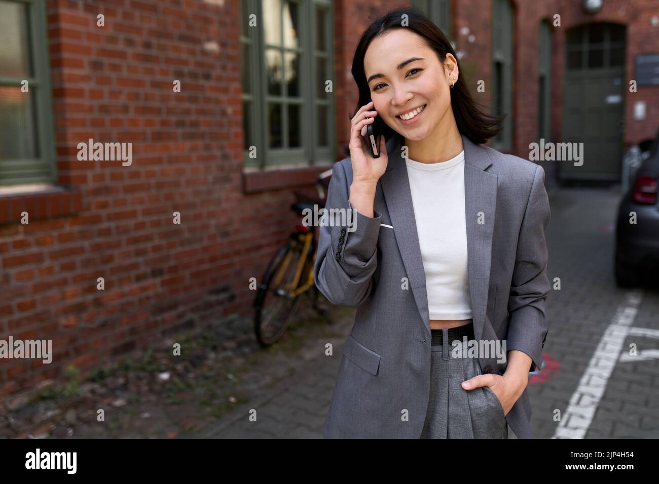 Lächelnde asiatische Geschäftsfrau, die draußen auf dem Mobiltelefon spricht. Stockfoto