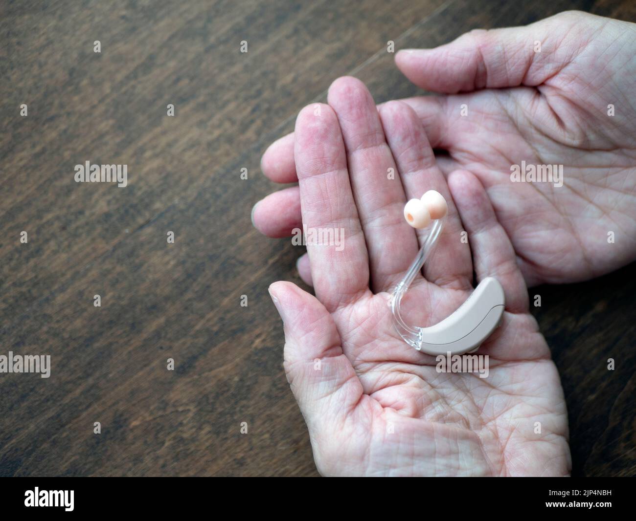 Zwei gealterte Hände halten ein Hörgerät, kopieren Platz. Konzept des Hörverlustes. Unterstützende Technologie Stockfoto