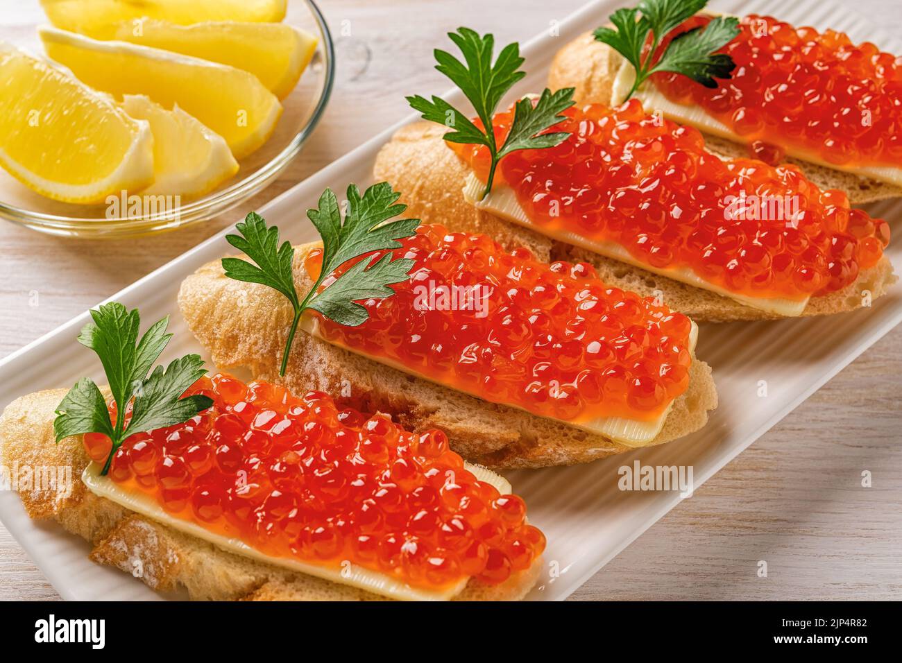 Sandwiches mit rotem Kaviar auf einem weißen Teller. Gourmet-Vorspeise mit Forellenkaviar auf einer Scheibe französischem Baguette mit Butter. Gesalzener Lachsrogen. Stockfoto