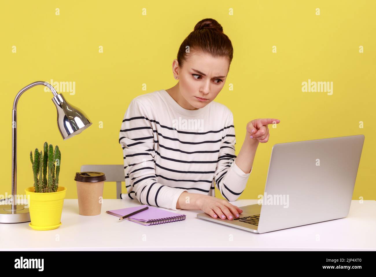 Seriöse Büroangestellte, die am Arbeitsplatz sitzt, schimpft, sagt, ich habe es Ihnen erzählt, sah auf einem Laptop-Display aus, während sie einen Videoanruf abgab. Studio-Innenaufnahme isoliert auf gelbem Hintergrund. Stockfoto