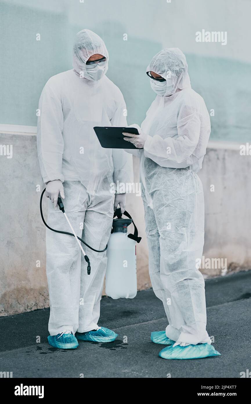 Mitarbeiter des Gesundheitswesens, die außerhalb eines Gebäudes reinigen, verwenden eine Liste, um Anweisungen zur Sicherheit von Biogefahren während des Einsatzes zu befolgen. Medizinische Forscher tragen Stockfoto